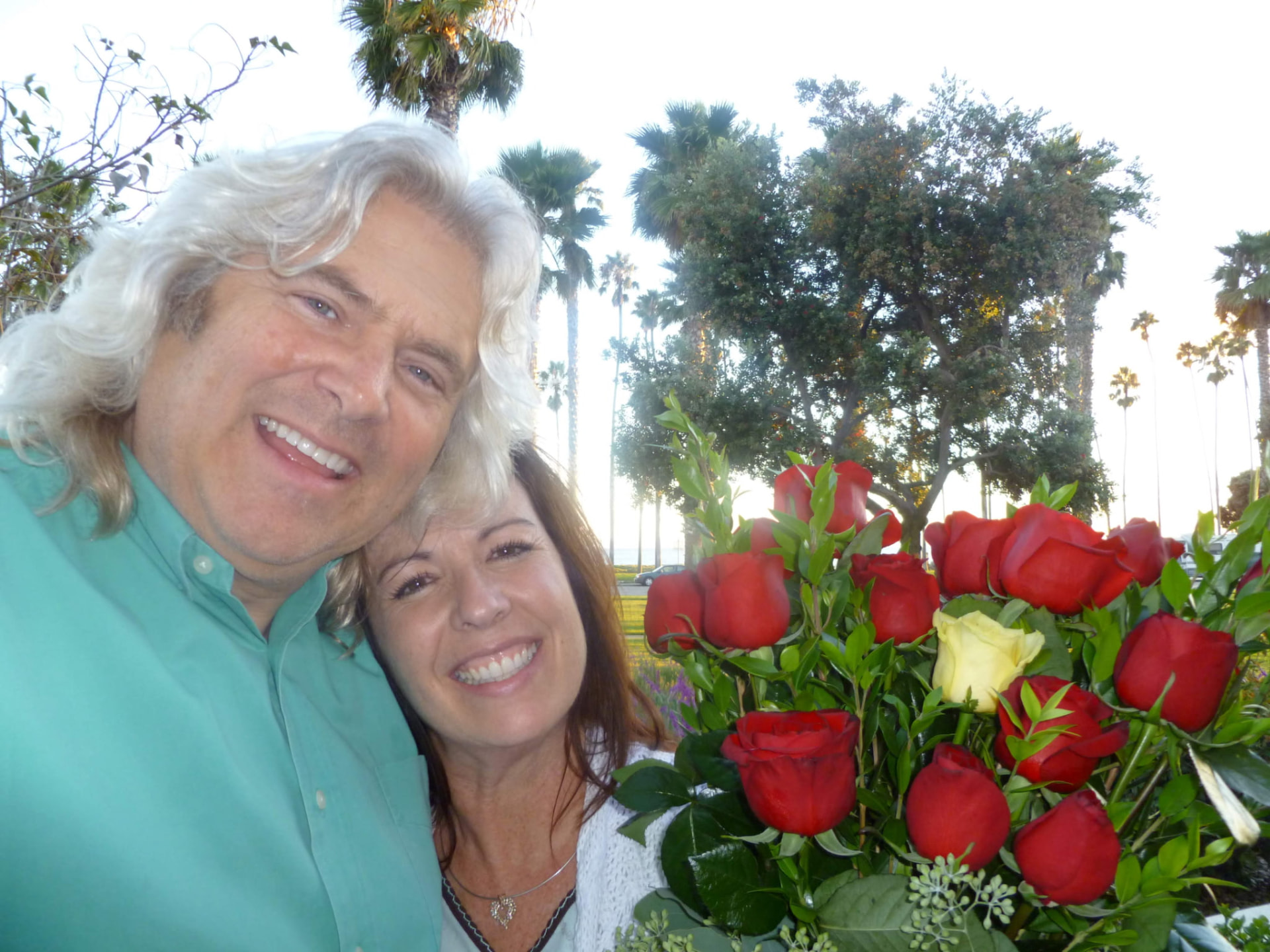 A smiling couple together holding a large bouquet of red roses