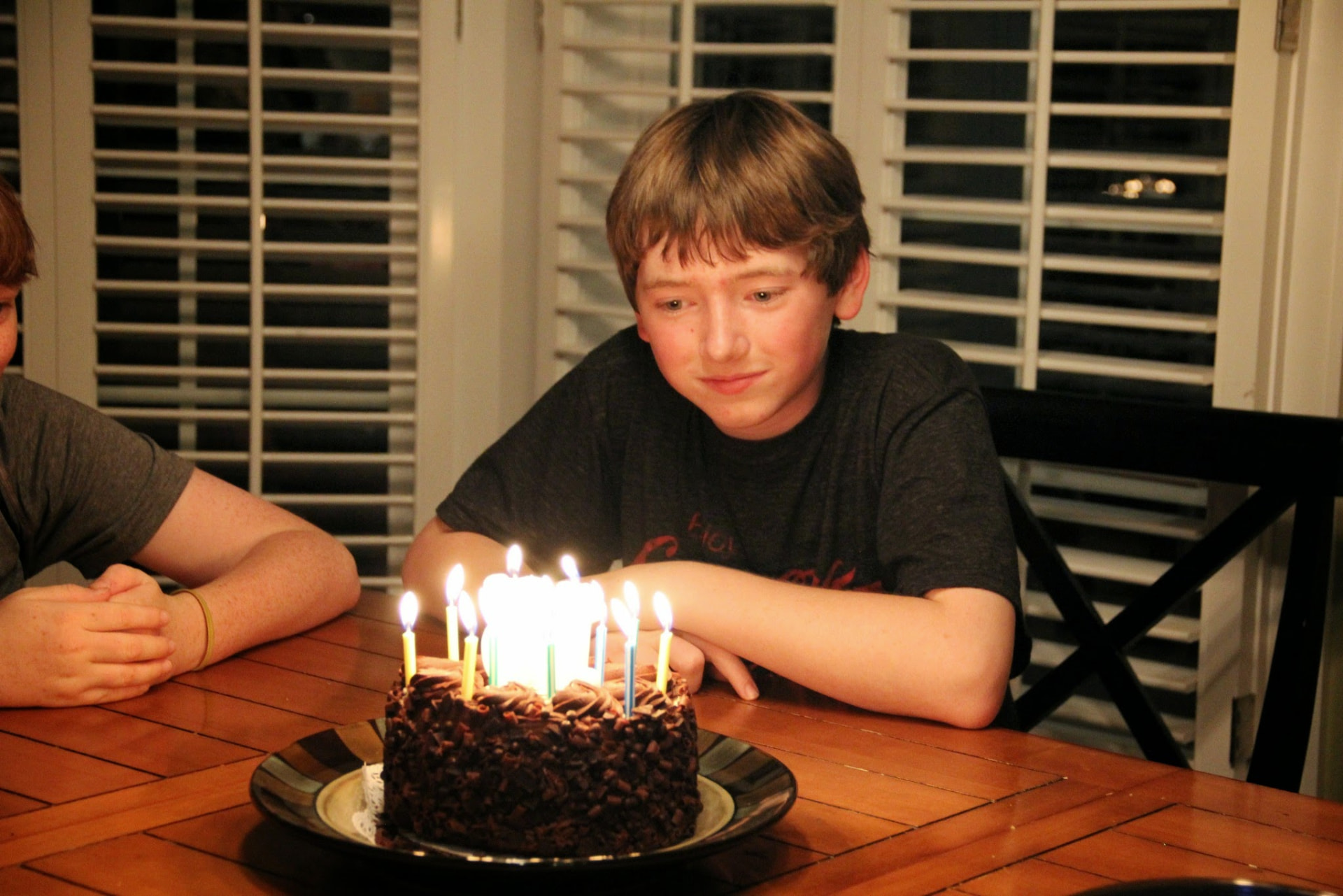 A boy smiling at a chocolate birthday cake lit with candles