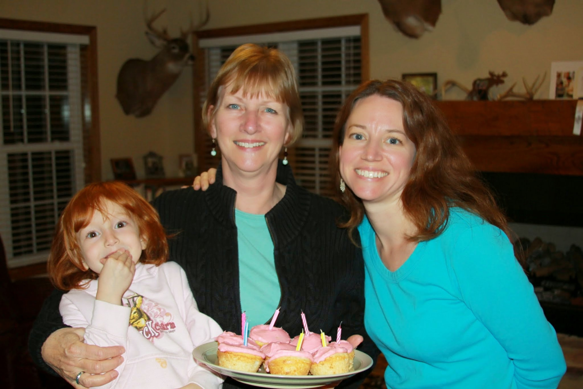 A grandmother, mother, and young girl holding a plate of birthday cupcakes