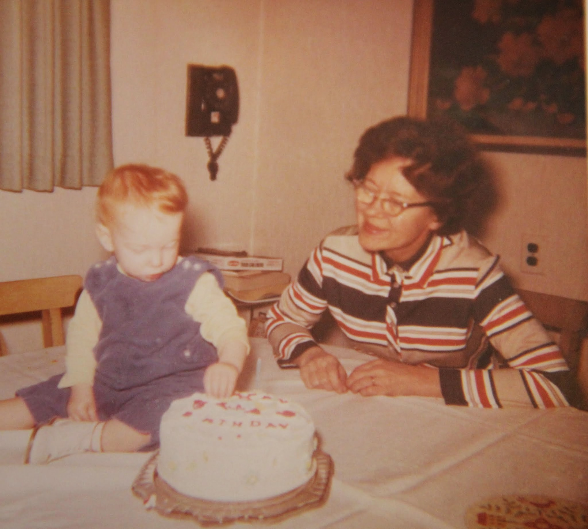 A vintage photograph of a toddler and his grandmother beside a birthday cake